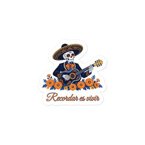 Peut inclure: Un autocollant découpé représentant un squelette vêtu d'un costume charro bleu foncé et d'un sombrero, jouant de la guitare acoustique. Le squelette est entouré de fleurs orange, avec le texte Recordar es vivir écrit en dessous.