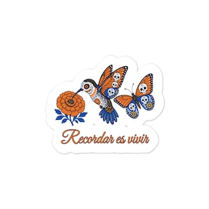 Peut inclure: Un autocollant découpé représentant un colibri et un papillon orange et bleu, ornés de motifs de crânes. Une fleur de souci orange est présente, et le texte Recordar es vivir est écrit en écriture cursive orange.