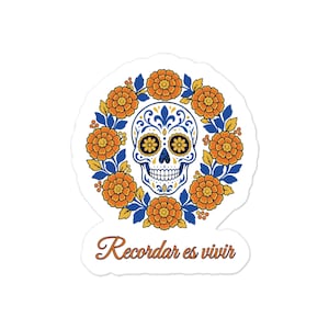 Peut inclure: Un autocollant découpé représentant un crâne en sucre blanc avec des motifs décoratifs bleus et jaunes, entouré d'une couronne circulaire de fleurs de souci orange et de feuilles bleues, avec le texte Recordar es vivir en dessous.