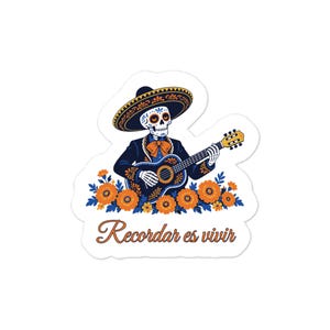 Peut inclure: Un autocollant découpé représentant un squelette vêtu d'un costume charro bleu foncé et d'un sombrero, jouant de la guitare. Le squelette est entouré de fleurs orange et du texte Recordar es vivir en écriture cursive brune.