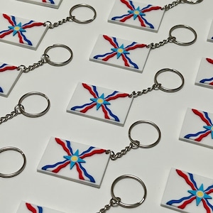 May include: Keyrings with a white rectangular design featuring a blue, red, and yellow starburst pattern. Each keyring has a silver-coloured chain and a round key ring. The keyrings are arranged on a white surface.