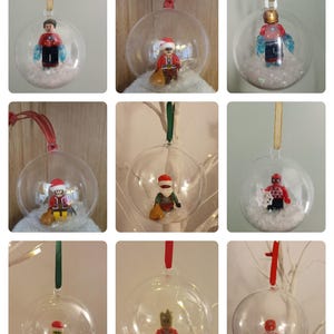 May include: Nine clear baubles, each containing a Lego figurine. The figurines include Santa Claus, superheroes, and other characters, set on faux snow. Each bauble has a ribbon for hanging on a Christmas tree.