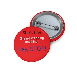 Puede incluir: Botón rojo con el texto "She's fine. She wasn't doing anything! Hey, STOP!" en negro y azul.