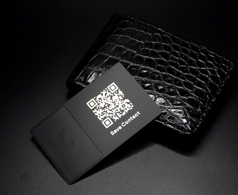 May include: A black business card with a QR code and the text "Save Contact" is displayed in front of a black leather wallet with a crocodile skin texture. The card has a rectangular design with a smooth, matte finish.