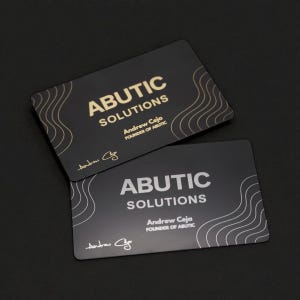 May include: Two black business cards with rounded corners. The cards feature the text "ABUTIC SOLUTIONS" in gold and white, with the name "Andrew Ceja" and the signature of Andrew Ceja. The cards have a wavy design.