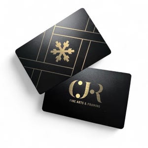 May include: Two black business cards with gold foil detailing. One card features a snowflake design, the other displays the initials "CJR" and the text "FINE ARTS & FRAMING". The cards are rectangular with rounded corners.