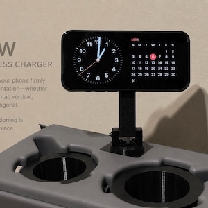 May include: A black wireless charger with a digital clock and calendar display. The charger is mounted on a gray base with two circular indentations. Text on the image reads "25W WIRELESS CHARGER". The display shows the month of May.