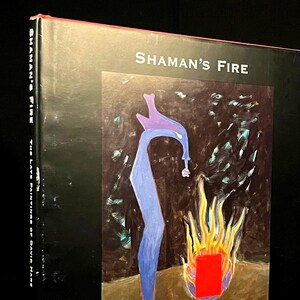 May include: A book titled "Shaman's Fire: The Late Paintings of David Hare" with a black cover and a colorful painting of a blue figure standing in front of a red box and flames on the front cover.