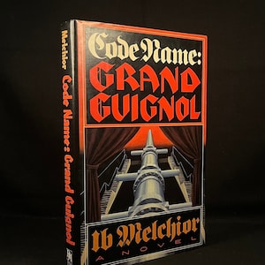 May include: A black and red book titled "Code Name: Grand Guignol" by W. Melchior. The cover features a stylized illustration of a stage with a large cannon pointed towards the viewer.