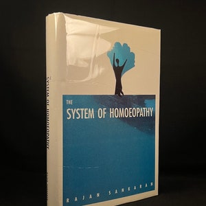 May include: The System of Homoeopathy book cover features a blue and white design with a silhouette of a person standing with arms raised. The text on the cover reads "The System of Homoeopathy" by Rajan Sankaran.