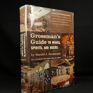 Peut inclure: Une couverture de livre avec un fond brun et un titre qui se lit "Grossman's Guide to Wines, Spirits, and Beers" par Harold J. Grossman. La couverture présente une photo d'une cave à vin avec des barils et une table avec des chaises.