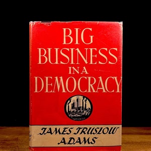 以下が含まれることがあります： ジェームズ・トラスロー・アダムズ著「民主主義における大企業」というタイトルの赤いハードカバーの本。本の表紙には、街並みの白黒イラストが描かれている。