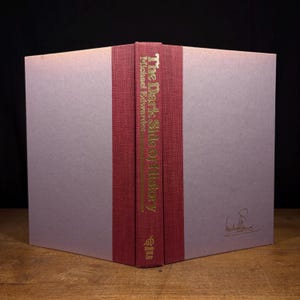 May include: A hardcover book titled "The Dark Side of History" by Michael Edwards. The spine is burgundy with gold lettering. The book's cover is a pale lavender color. The book is displayed open, revealing the spine and part of the cover.