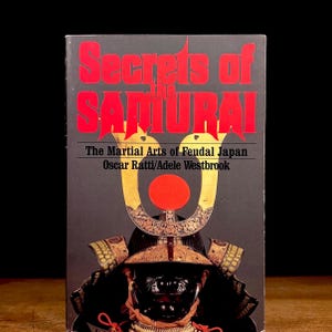 May include: A book titled "Secrets of the Samurai" with red lettering on a dark gray background. The book cover features a detailed illustration of samurai armor and helmet, with the text "The Martial Arts of Feudal Japan" and author names.