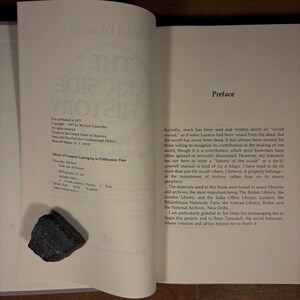 May include: Open book with text and a dark gray rock on the left page. The book's title is "The Dark Side of History" by Michael Edwardes. The right page has a preface. The book is printed in the United States.