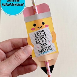 Può includere: Una carta di carta a forma di matita gialla con una gomma rosa in alto e una punta nera. La carta presenta un volto sorridente e un biglietto bianco con il testo "LET'S START THE YEAR OFF WRITE!". Una matita decorata è inserita nelle fessure.