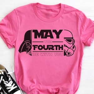 Peut inclure: T-shirt rose avec un motif noir représentant Dark Vador et un Stormtrooper. Le texte dit "Que la force soit avec toi".