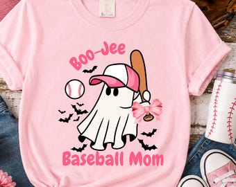 May include: A light pink t-shirt featuring a graphic of a white ghost wearing a pink and white baseball cap. The ghost holds a brown baseball bat with a pink bow. The text reads Boo-Jee Baseball Mom, surrounded by small black bats and a baseball.