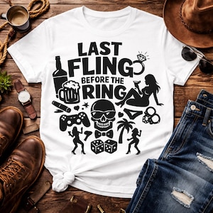 May include: White t-shirt with a black graphic design that includes the text "LAST FLING BEFORE THE RING". The design features a skull, dice, a ring, and silhouettes of people.