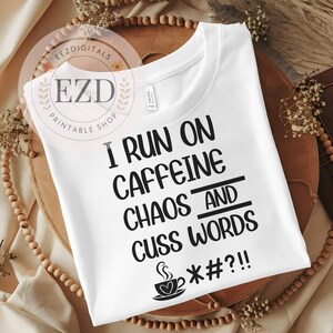 May include: White t-shirt with the text "I RUN ON CAFFEINE CHAOS AND CUSS WORDS" in black. A coffee cup graphic is below the text. The shirt is a crew neck style.