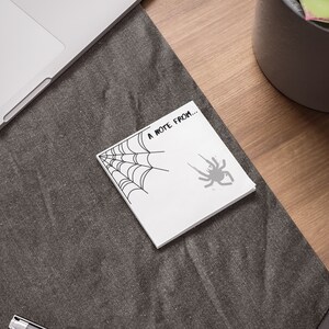 May include: A white note with a black spider web and spider illustration. The note says "A note from..."