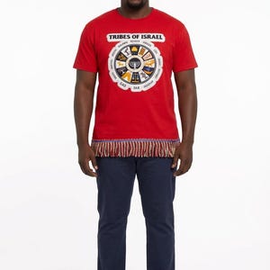May include: A red t-shirt with the text "TRIBES OF ISRAEL" and a circular graphic. The graphic features symbols and text. The shirt has a decorative fringe at the bottom. The person is wearing navy blue pants and white sneakers.