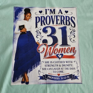 May include: A light mint green t-shirt featuring a graphic print of a person in a white long-sleeve top and a blue fringed skirt holding a book. The text reads I'M A PROVERBS 31 Women, SHE IS CLOTHED WITH STRENGTH & DIGNITY; SHE CAN LAUGH AT THE DAYS TO COME.