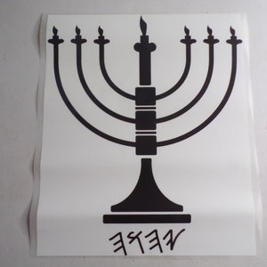 Puede incluir: Una menorá negra con siete velas, una vela central y una base. La menorá está sobre un fondo blanco con la palabra "SHAN" escrita debajo.