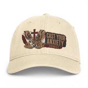 Puede incluir: Una gorra de béisbol color crema con un estampado gráfico de dos manos soltando piedras bajo una cruz. El texto CAST YOUR ANXIETY y 1 PETER 5:7 aparece en letras de color marrón oscuro sobre un fondo rectangular texturizado.