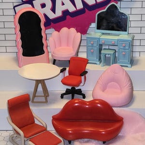 Puede incluir: Un conjunto de muebles en miniatura, que incluye un tocador con espejo, un sillón rosa, una silla de oficina roja, un sillón de frijoles rosa, un sillón rojo con un reposapiés, un sofá rojo en forma de labios, una mesa blanca y una alfombra rosa.