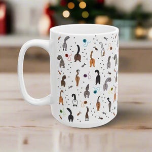 May include: White ceramic coffee mug with a pattern of cats' rear ends and tails. The cats are in various colors and poses, with some holding yarn or fish.
