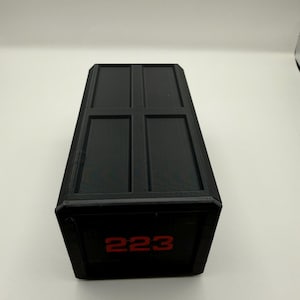 May include: A black rectangular box with a textured surface and a hinged lid. The front of the box displays the number "223" in red. The box has a simple, geometric design.