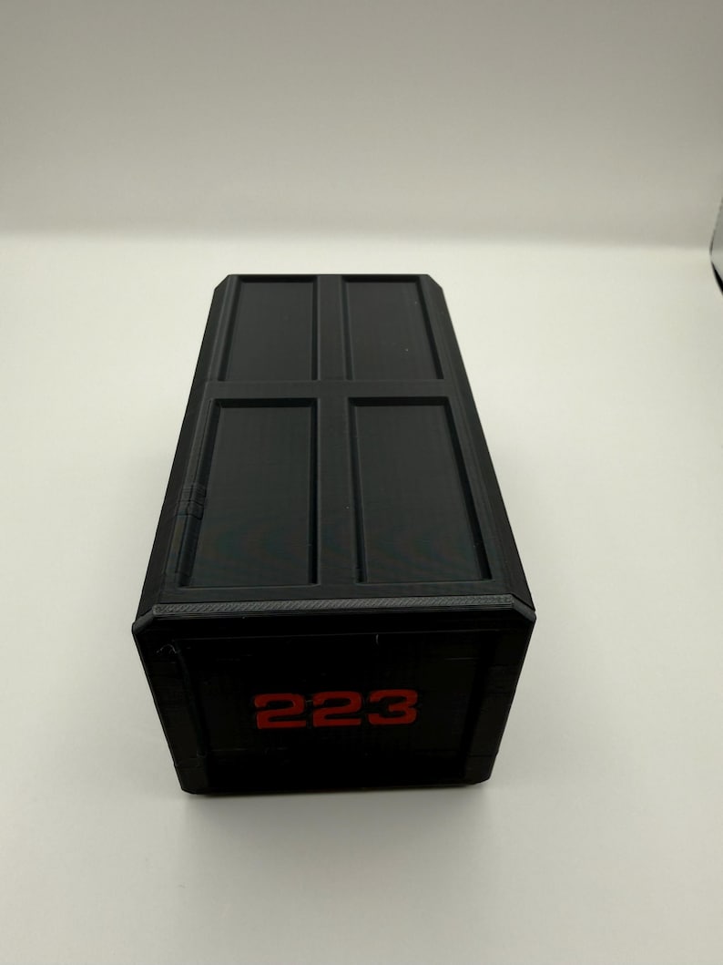 May include: A black rectangular box with a textured surface and a hinged lid. The front of the box displays the number "223" in red. The box has a simple, geometric design.