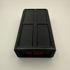 May include: Black rectangular case with a textured surface and a grid-like design on the top. The text "40 S&W" is printed in red on the front of the case.