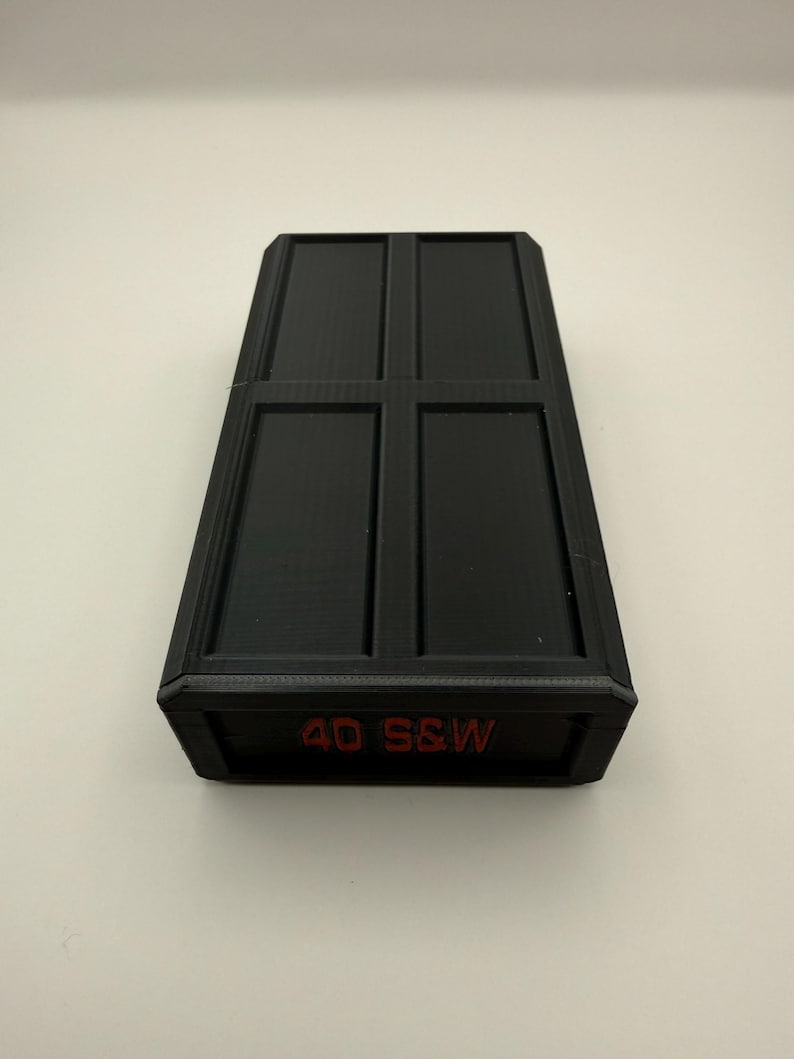 May include: Black rectangular case with a textured surface and a grid-like design on the top. The text "40 S&W" is printed in red on the front of the case.