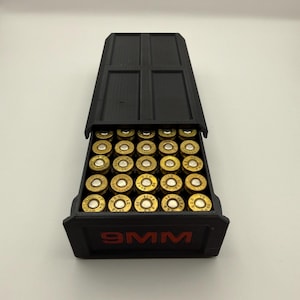 May include: A black 9MM ammunition storage box with a hinged lid, filled with brass-colored bullets. The box has red lettering that reads "9MM". The bullets are neatly arranged inside the box.