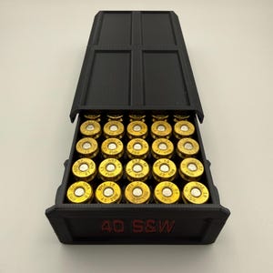 May include: Black 3D-printed ammunition box with a hinged lid, open to reveal rows of gold-colored bullets. The box is labeled "40 S&W" in red lettering, indicating the ammunition type. The bullets are arranged neatly inside.