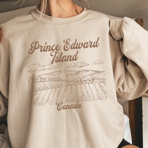 May include: A beige sweatshirt with a brown graphic print of a landscape with the text "Prince Edward Island, Canada".
