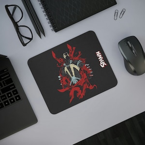 May include: A black and red mousepad with a graphic of Spawn, a comic book character, in a red cape. The text "Spawn" is printed in white on the mousepad.