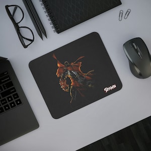 May include: A black mouse pad with a red and black illustration of Spawn, a comic book character, with the word "SPAWN" in white text in the bottom right corner.