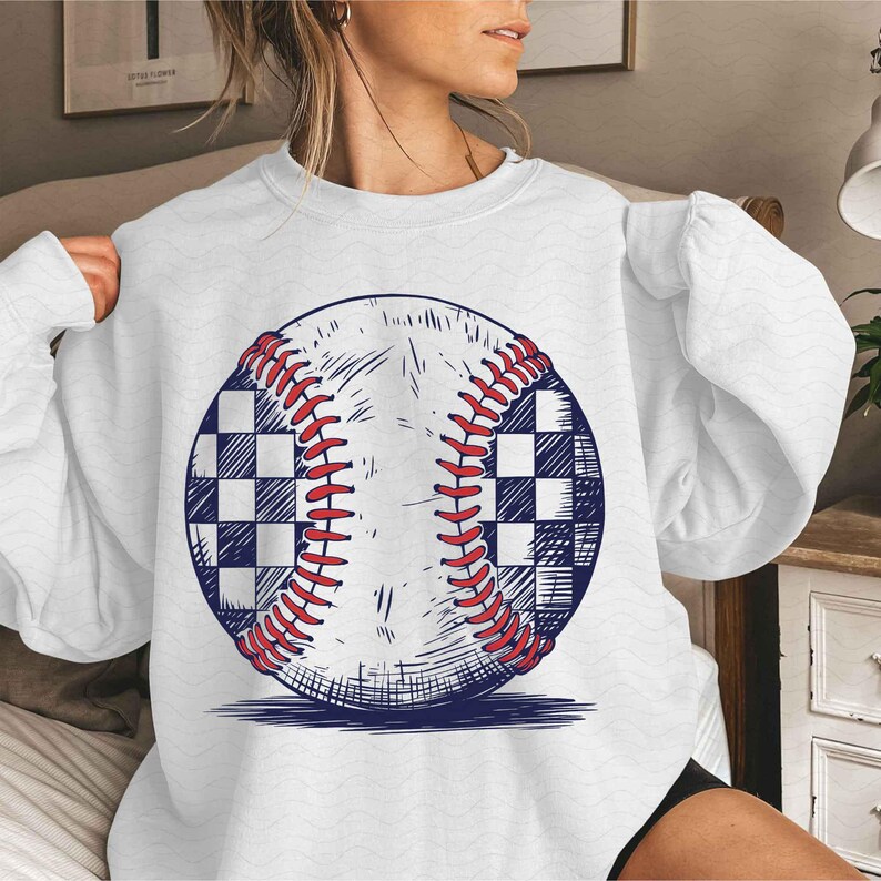 Puede incluir: Sudadera blanca con un gr&aacute;fico de una pelota de b&eacute;isbol con un patr&oacute;n a cuadros. La pelota de b&eacute;isbol est&aacute; dibujada en un estilo vintage.