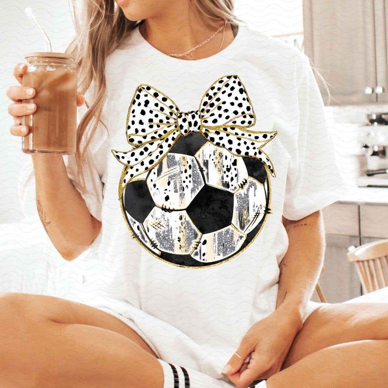 May include: White t-shirt with a black and white polka dot bow on top of a black and white soccer ball.