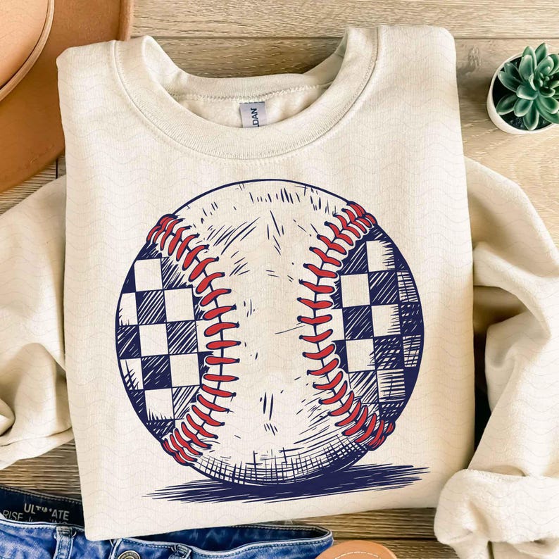 Puede incluir: Una sudadera de color crema con un gr&aacute;fico de b&eacute;isbol a cuadros en blanco y negro. La pelota de b&eacute;isbol tiene costuras rojas.