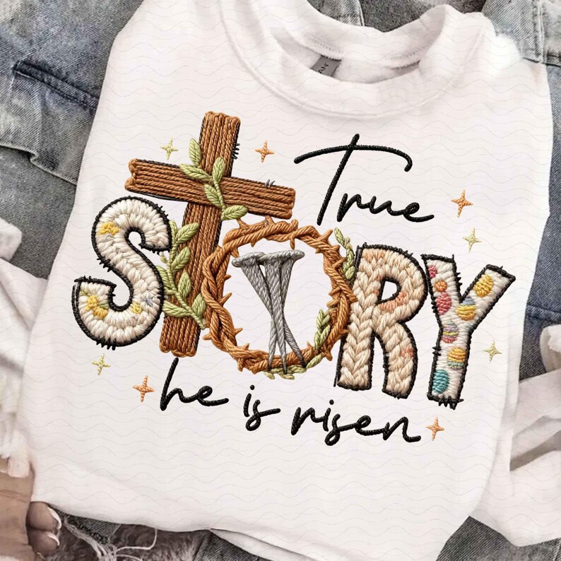 Puede incluir: Sudadera blanca con dise&ntilde;o bordado. Presenta una cruz marr&oacute;n, una corona de espinas con clavos y las palabras "True Story" en una fuente decorativa. Tambi&eacute;n incluye la frase "he is risen". Acentuado con peque&ntilde;os detalles de estrellas.