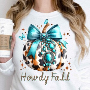 May include: White sweatshirt with a turquoise and brown pumpkin with a turquoise bow and jewels. The text "Howdy Fall" is printed below the pumpkin.