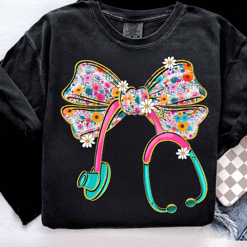 Peut inclure: Sweat-shirt noir avec un n&oelig;ud floral et un motif de st&eacute;thoscope. Le n&oelig;ud est orn&eacute; de fleurs roses, oranges et bleues. Le st&eacute;thoscope est rose et turquoise, avec des accents de marguerites, cr&eacute;ant un design sur le th&egrave;me m&eacute;dical.