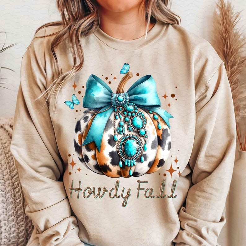 May include: A tan sweatshirt with a graphic of a turquoise and brown pumpkin with a turquoise bow and turquoise jewels. The text "Howdy Fall" is printed below the pumpkin.