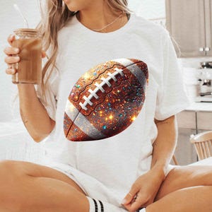 May include: A white t-shirt with a glittery brown and white football design.