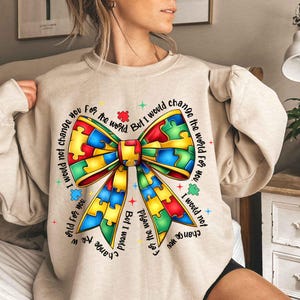 May include: A beige sweatshirt with a colorful puzzle piece bow and the text "I would not change you for the world. But I would change the world for you."