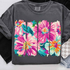 May include: A charcoal grey t-shirt with a floral print design. The flowers are pink, white, and blue with a teal green background. The design is in a vertical stripe pattern.